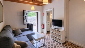 A modern living room with a grey sofa, a small white table, a TV on a white stand, and a patterned floor. - La Curuxa House in Vidiago, Llanes (Vidiago)