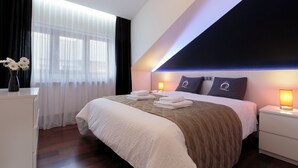 Una habitación de hotel moderna con una cama grande, una mesita de noche y una ventana con cortinas translúcidas.