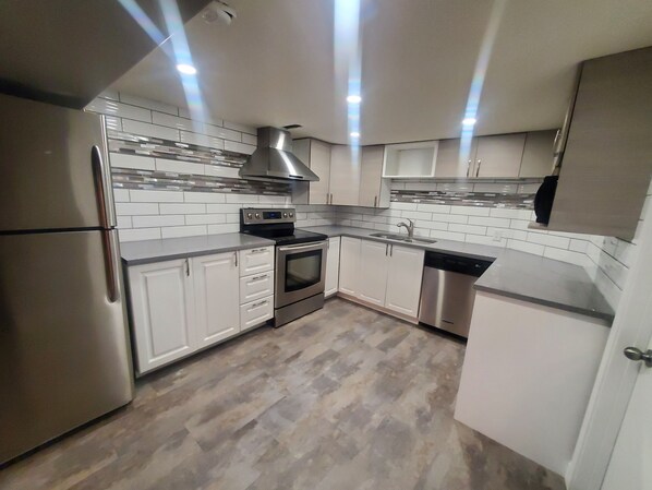 A modern kitchen with stainless steel appliances, white cabinetry, and a herringbone tile backsplash.
