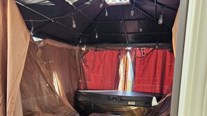 A compact living space with a kitchenette, a small table, a sofa, and a tent-like structure with a red curtain. - For a professional Room in NW Calgary (Calgary)