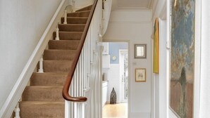 Un pasillo con una escalera con alfombra, un candelabro colgante y un cuadro en la pared.