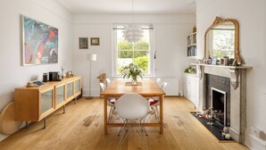 Un comedor con una mesa de madera, sillas blancas, una chimenea y una estantería.
