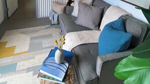 A modern living room with a grey sofa, a flat-screen TV mounted on the wall, a lamp, and a painting. - Unique container home  (El Cajon)