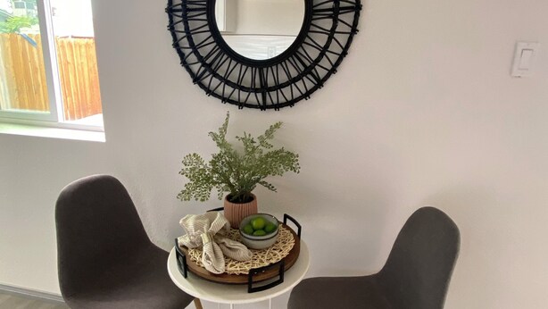 A room with two dark chairs, a small white table with a plant and a bowl, and a large black circular mirror on the wall. - Unique container home  (El Cajon)