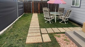 Un jardin avec une table et des chaises de patio, un parasol à rayures et un chemin de pierres.