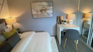 Une chambre moderne avec un lit, des lampes de chevet, un bureau avec une chaise, un miroir et un tableau abstrait accroché au mur.
