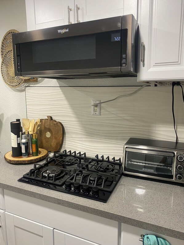 A kitchen with a Black & Decker toaster oven, a stove, and a microwave above it. - Unique container home (El Cajon)