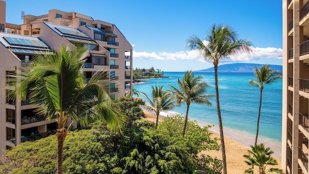 Ein Strandhotel mit mehreren Balkonen mit Blick aufs Meer, einem klaren Himmel und tropischer Vegetation.