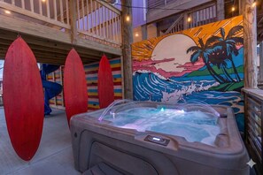 Un bain à remous agrémenté d’une fresque représentant un coucher de soleil et de planches de surf, le tout installé sur une terrasse en bois.