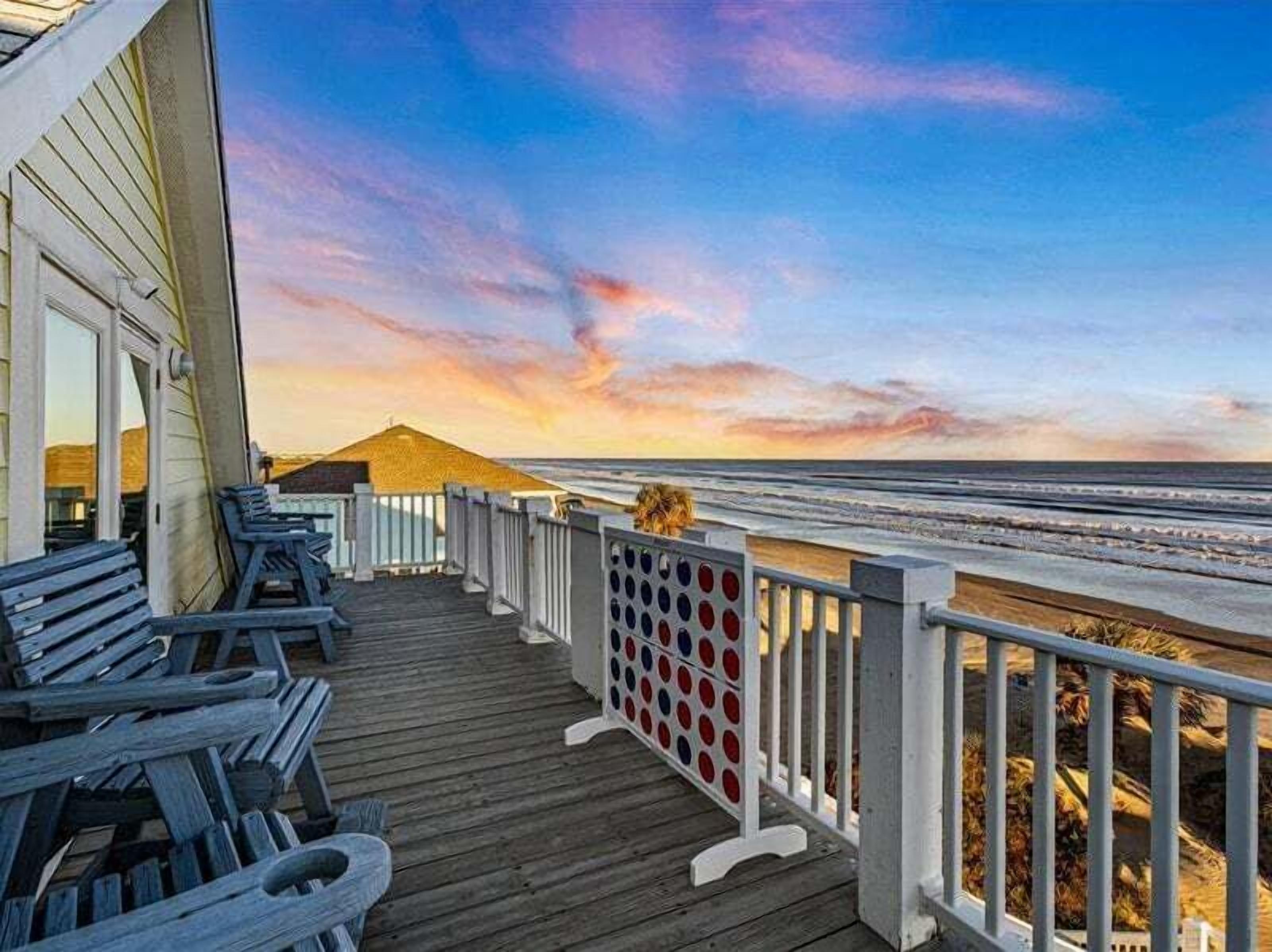 Una terraza de madera con vista al océano y al atardecer.