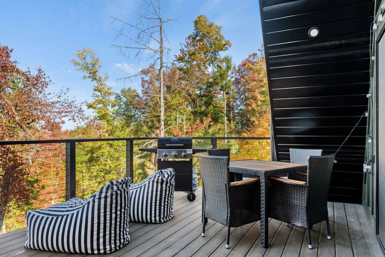 Une terrasse dotée d'un barbecue, de meubles en osier et offrant une vue sur les arbres aux couleurs automnales.