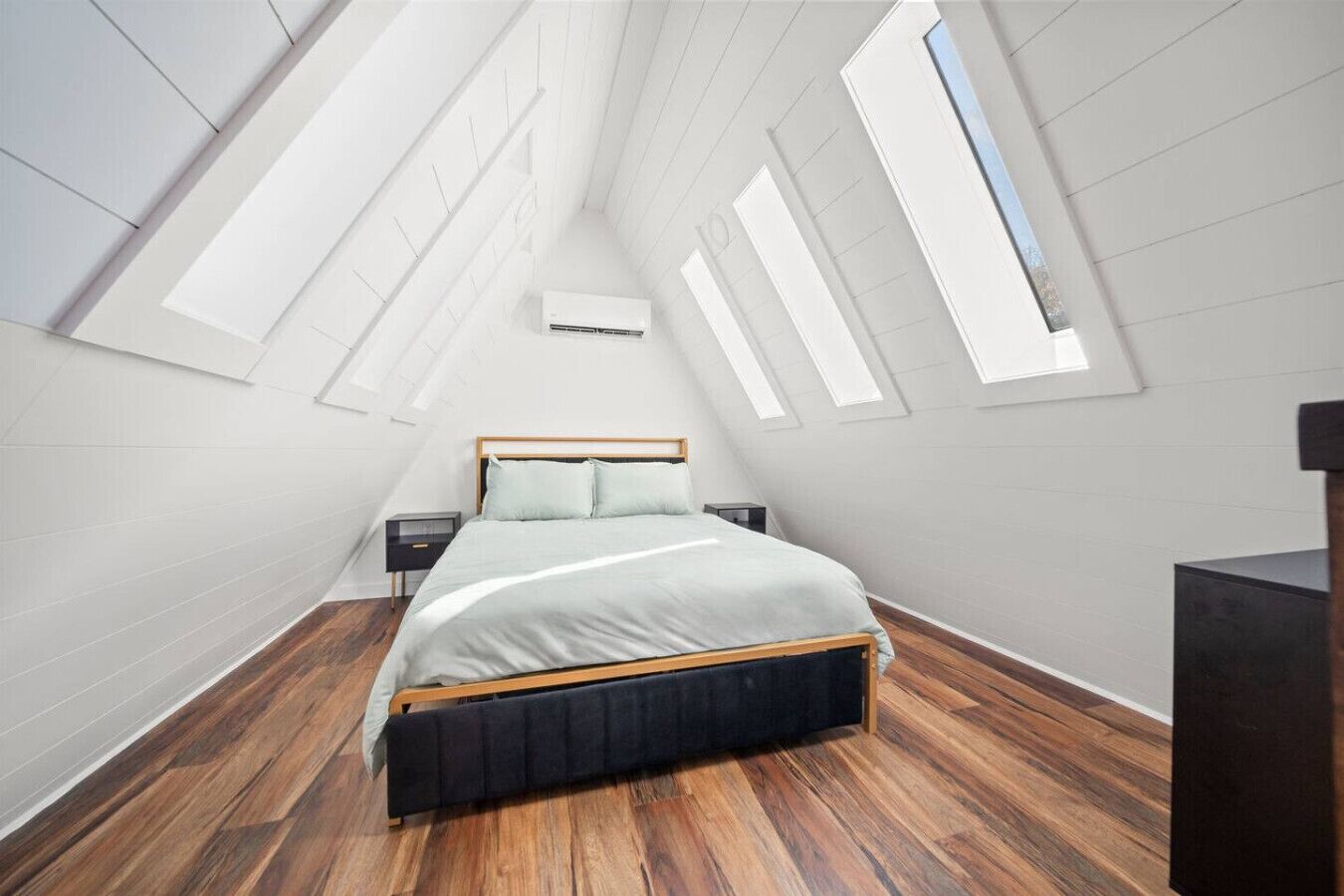 Une chambre avec un plafond en pente, des fenêtres de toit, un lit, une table de chevet et une commode.