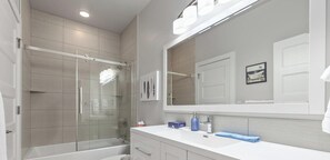 A modern bathroom with a glass-enclosed shower, a large mirror, and a white vanity.