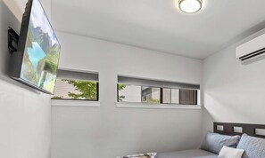 A bedroom with a bed, a TV mounted on the wall, and two windows. - Modern Ground-Level Condo Downtown—Perfect Walkability & Shared Outdoor Space for Relaxation! (Coeur D Alene)