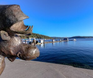 A sculpture of a large animal near a waterfront with boats and a dock in the background.
