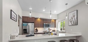 A modern kitchen with a large island, stainless steel appliances, pendant lighting, and artwork on the walls. - Modern Ground-Level Condo Downtown—Perfect Walkability & Shared Outdoor Space for Relaxation! (Coeur D Alene)