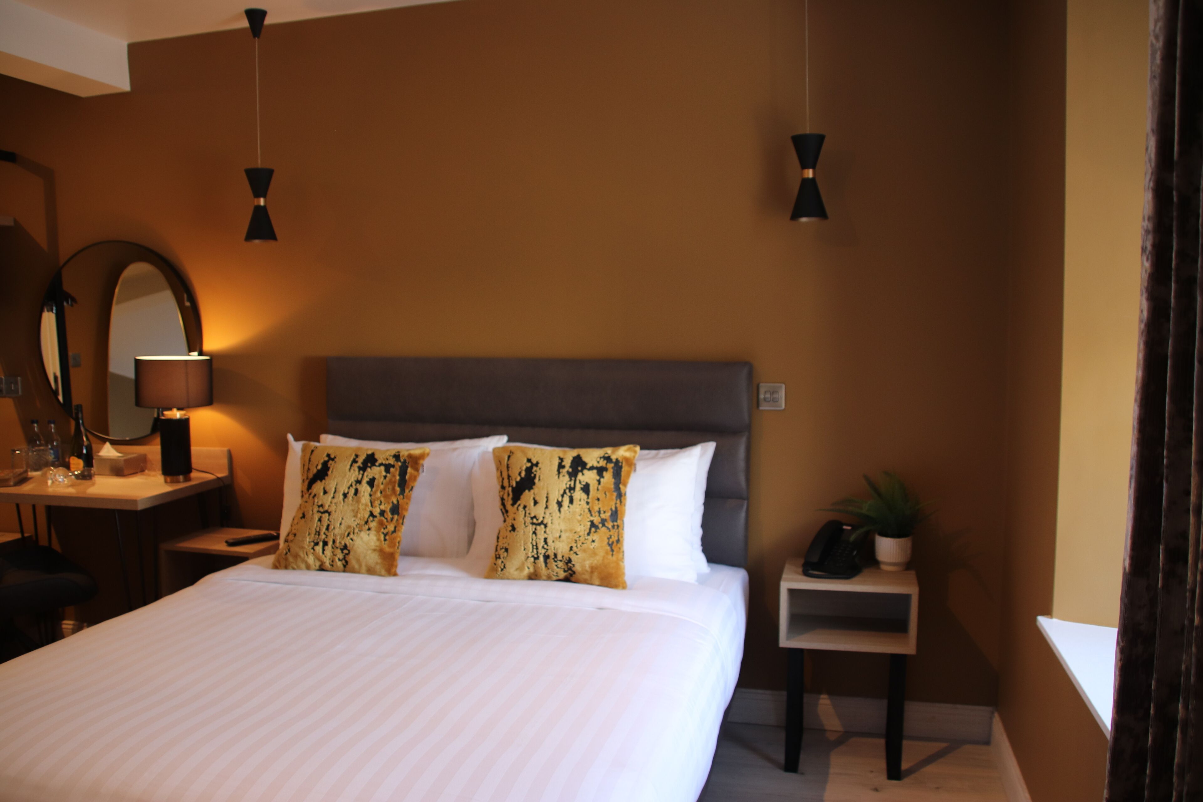 Une chambre d’hôtel avec un grand lit, des tables de chevet, un bureau avec une lampe, un miroir et une plante en pot.