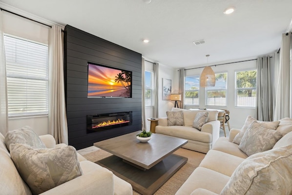 A modern living room with a fireplace, a flat-screen TV, and a sofa set. - Beachside Deluxe: Private Pool, Theater, Golf, Games & Endless Amenities 🌴 (Melbourne Beach)