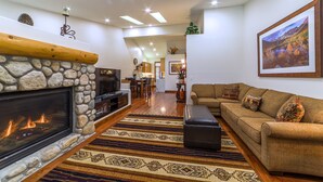 A spacious living room with a stone fireplace, a large sofa, and a dining area in the background. - Bright, Newly Remodeled 2/2 w/ Garage & Laundry! (Mammoth Lakes)