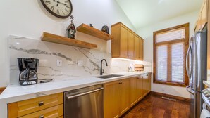 A kitchen with marble countertops, wooden cabinets, a stainless steel dishwasher, and a clock on the wall. - Bright, Newly Remodeled 2/2 w/ Garage & Laundry! (Mammoth Lakes)