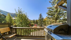 A balcony with a grill, wooden bench, and a view of trees and mountains. - Bright, Newly Remodeled 2/2 w/ Garage & Laundry! (Mammoth Lakes)
