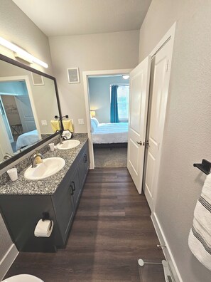 A hotel bathroom with a double sink, a large mirror, a toilet, and a shower area.