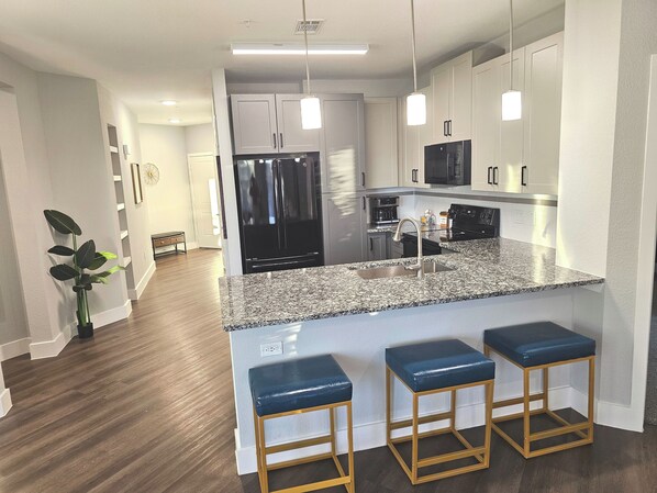 A modern kitchen with granite countertops, stainless steel appliances, and a central island with bar stools. - Lux 2 Bedroom king+twin trundle room, Pool views (Lewisville)