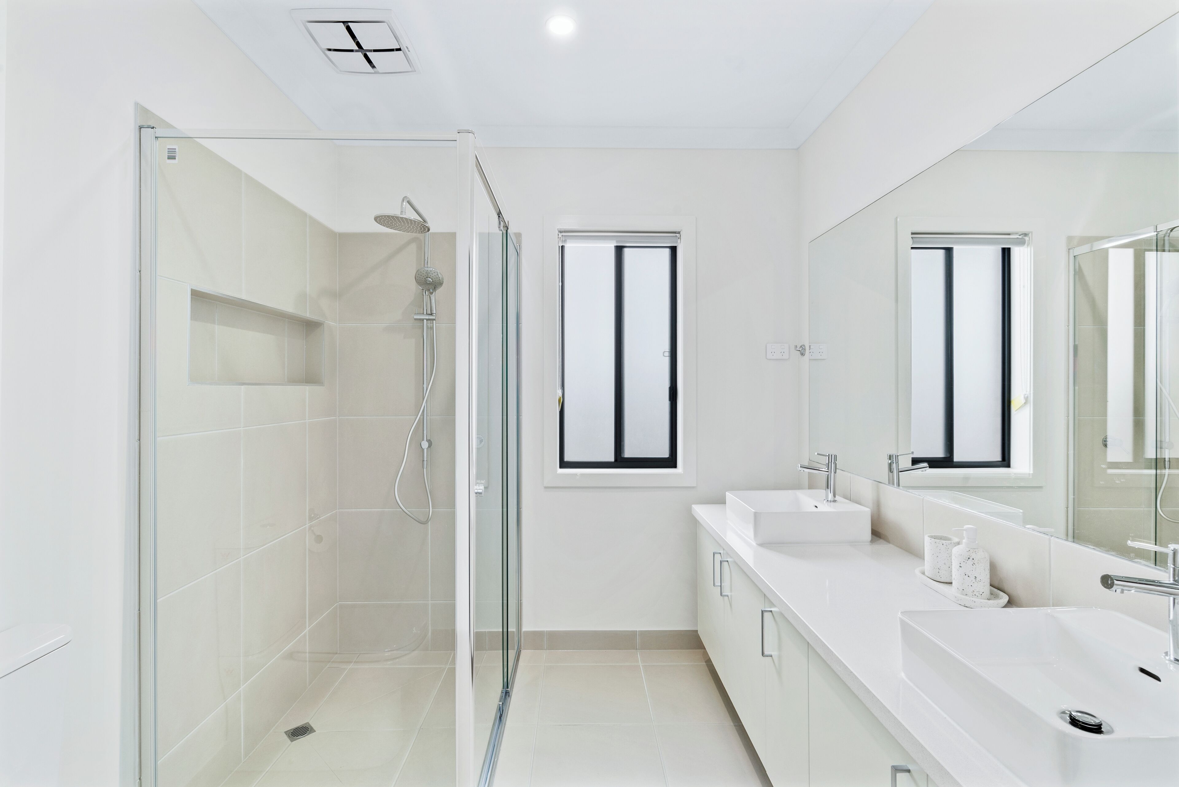 Een moderne badkamer met een douchecabine van glas, een grote spiegel en een wit wastafelmeubel met twee wasbakken.