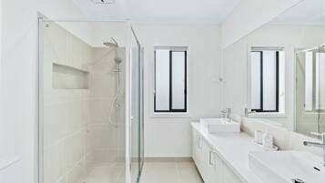 Een moderne badkamer met een douchecabine van glas, een grote spiegel en een wit wastafelmeubel met twee wasbakken.