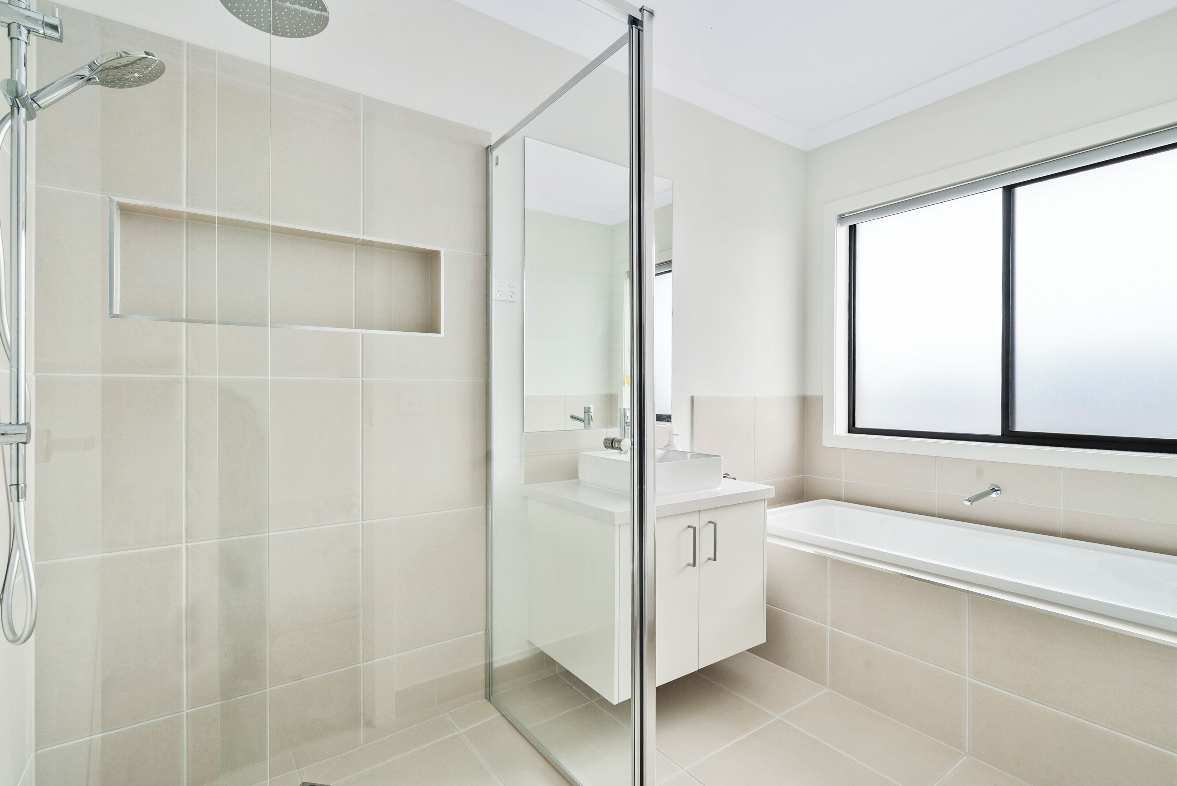 Een moderne badkamer met een douchecabine van glas, een wit wastafelmeubel en een groot raam.