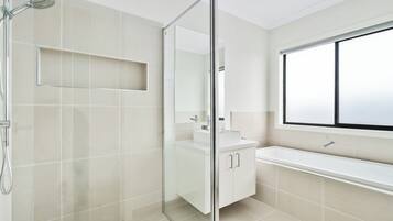 Een moderne badkamer met een douchecabine van glas, een wit wastafelmeubel en een groot raam.