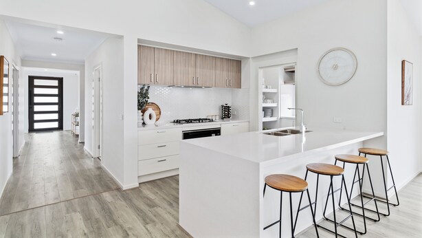 A modern kitchen with white cabinetry, a large island with bar stools, and a view into the adjacent living area.
