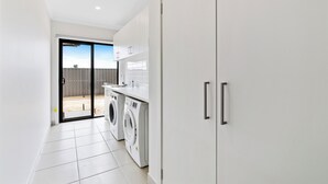 A laundry room with a washing machine and dryer, a sliding glass door leading to an outdoor area, and white cabinets with handles.