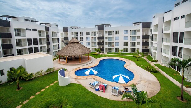 Ein Resort mit einem zentral gelegenen Swimmingpool, Liegestühlen und einem Pavillon mit Reetdach.