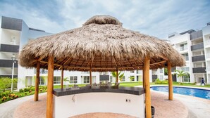 Ein mit Strohdach versehenes Freiluftbar-Gelände mit Pool im Hintergrund.