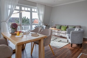 A modern living room with a wooden dining table, grey armchairs, and a grey sofa with green cushions.