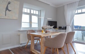 A modern dining area with a wooden table and four chairs, a television, and a view of the city through large windows.