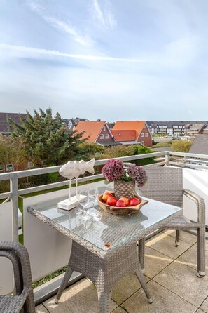 Ein Balkon mit Korbmöbeln, einem Glastisch, dekorativen Fischen und einer Obstschale.