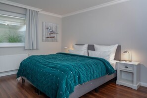 A bedroom with a teal bedspread, a nightstand with a lamp, and a window with curtains.