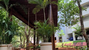 Un espacio al aire libre cubierto con suelo de madera, macetas grandes y una hamaca.