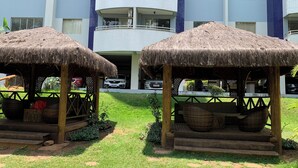 Un hotel con dos construcciones de techo de paja, un estacionamiento y un edificio de varios pisos con balcones.