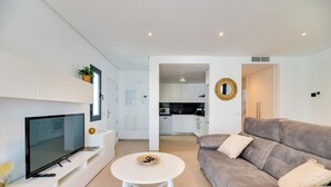 A modern living room with a flat-screen TV, a white coffee table, and a grey sofa.