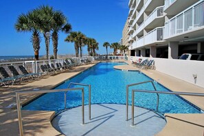 A swimming pool with sun loungers and palm trees, surrounded by a white building with balconies. - Stunning Oceanfront 3 Bedroom 3 Bath Condo - Crescent Shores North Myrtle Beach (North Myrtle Beach)