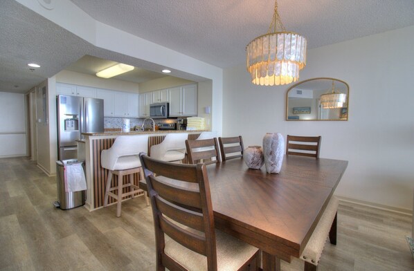 Un comedor espacioso con una mesa y sillas de madera, un candelabro y una cocina al fondo.