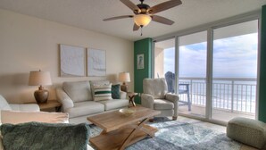 A spacious living room with a large window offering a view of the ocean, a ceiling fan, and a wooden coffee table.