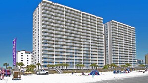 A multi-story hotel with balconies, located near a beach.