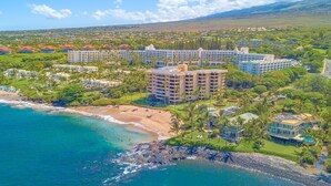 Una località balneare con proprietà fronte spiaggia, un edificio centrale su più piani e vegetazione circostante.