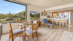 Una cucina moderna con elettrodomestici in acciaio inossidabile, un'area pranzo con sedie in vimini e un'ampia finestra con vista su un paesaggio suggestivo.