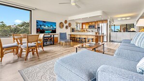Un soggiorno moderno con una grande TV, zona pranzo, cucina e un balcone con vista.