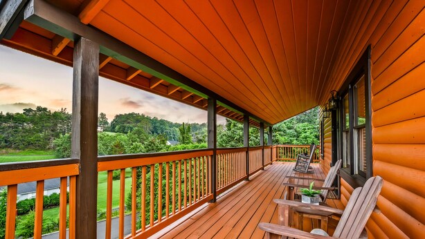 Una terraza de madera con barandilla, sillas y una mesa.